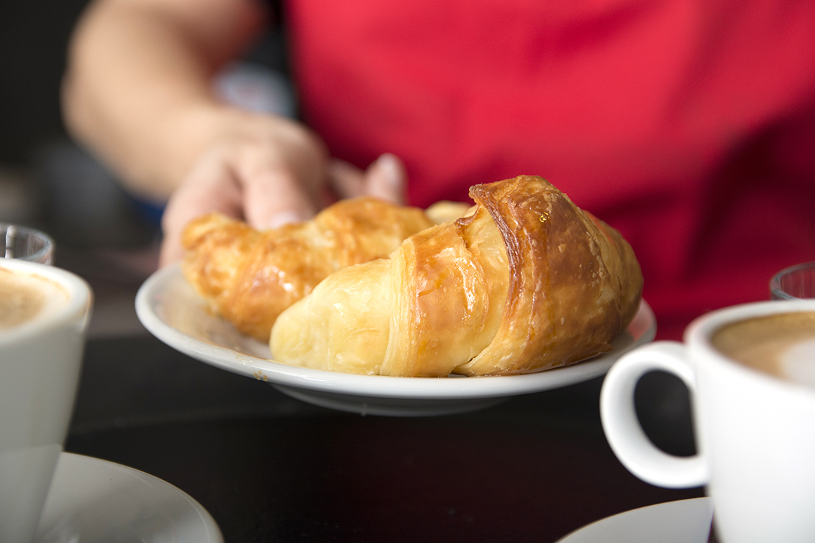 Waitress s hand offering fresh baked croissant plate resized